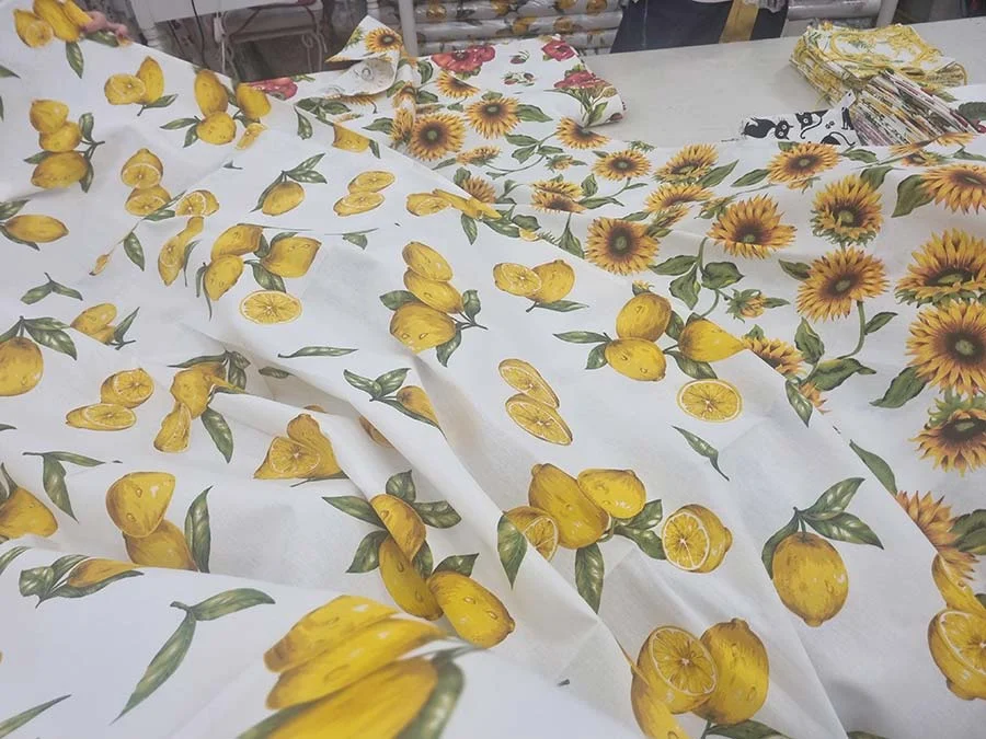 Cream linen printed with yellow lemons and green leaves, with sunflower print fabric beyond, laid out on a table