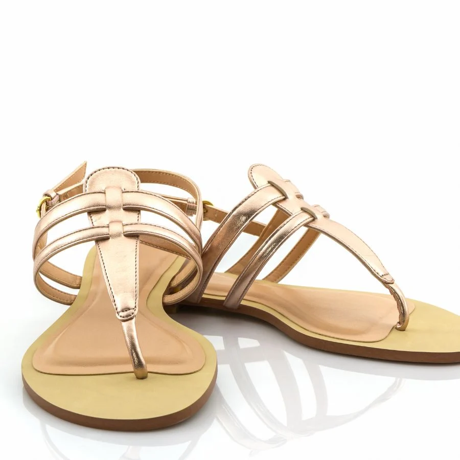 Pair of metallic rose-gold flat sandals with T-bar straps and ankle buckles, on a white background