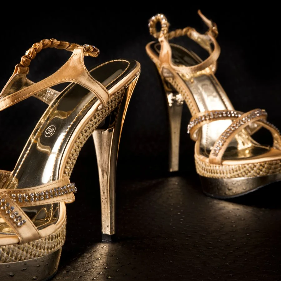 Gold high-heeled sandals with jewelled straps and platform soles, on a black background