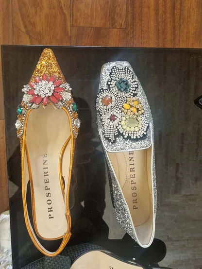 Prosperine flats on a black display: a gold glitter slingback and a silver glitter flat, both with jewelled flowers