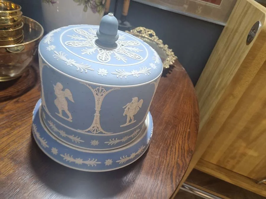 Cheese keeper from the front, showing white cupids between ornamental columns under an acorn-shaped knob