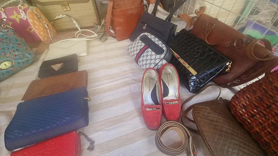 Handbags, purses and a pair of red loafers laid out on a striped cloth at a bag stall