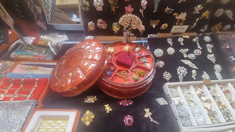 Vintage brooches in rhinestone, flower and fan shapes pinned to black cloth, beside an open red round box of pins