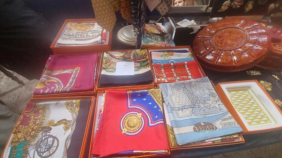 Printed silk scarves laid out in orange boxes beside a round red lacquer-look case