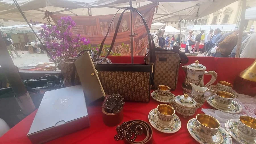 Two vintage monogram canvas handbags on a red cloth with gold-rimmed teacups, a teapot and a belt