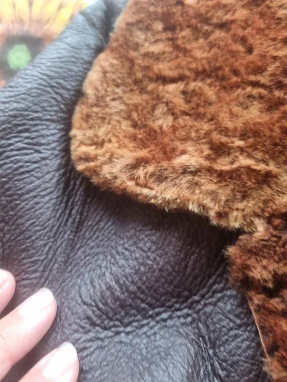 Dark brown leather shearling collar turned back to show orange-brown fleece lining, held in a hand