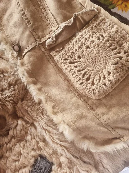 Crochet pocket and stitched seams on a cream shearling jacket, with fleece showing at the edge