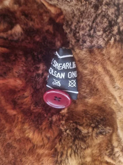 Care label inside a russet shearling coat, next to a dark red button