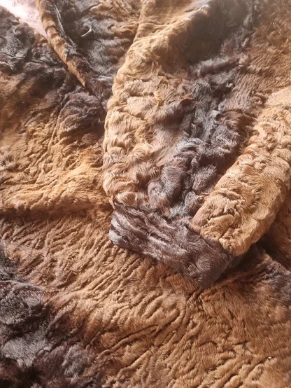 Curly brown and black fur coat laid flat, showing the textured pile and a sleeve cuff