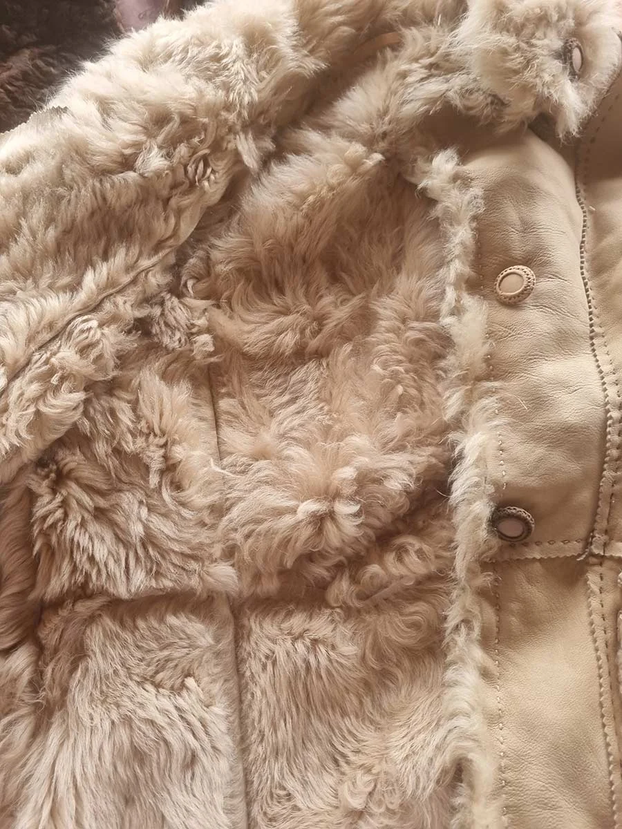 Cream shearling jacket open to show its thick fleece lining and two brass-coloured buttons