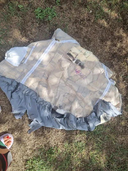 Fur coat laid flat on grass with the lining peeled back to show the beige leather backing and white seam tapes