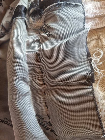 Grey silk lining with repeated lettering, hand-stitched with black thread, next to the pelt backing