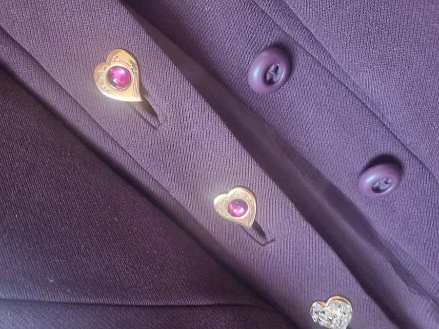 Yves Saint Laurent heart-shaped gold earrings with pink stones clipped down the front of a plum wool jacket
