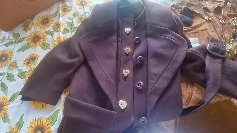 Plum wool jacket laid out on a sunflower cloth, with heart-shaped Yves Saint Laurent earrings clipped on as brooches