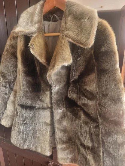 Short seal fur jacket with a notched collar, hanging against a dark wooden door