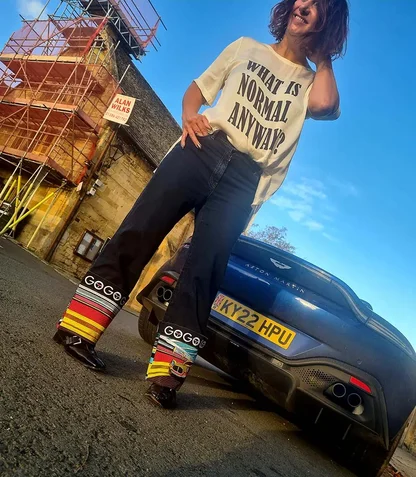 Gracie Opulanza in a printed T-shirt and jeans with striped embroidered hems, beside a dark blue Aston Martin