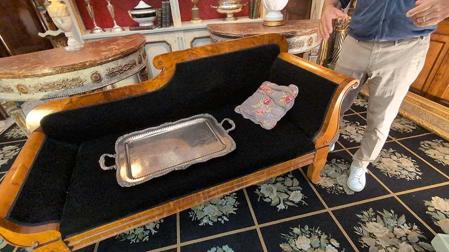 Antique wooden-framed sofa upholstered in black velvet, with a silver tray and a floral cushion, on a patterned tiled floor