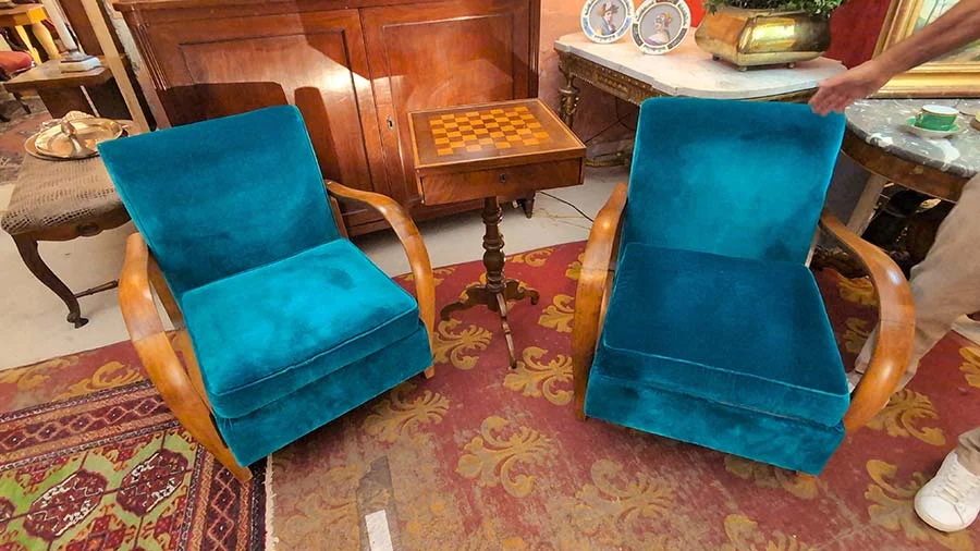 Pair of refurbished armchairs in teal velvet with curved wooden arms, beside a small inlaid chess table