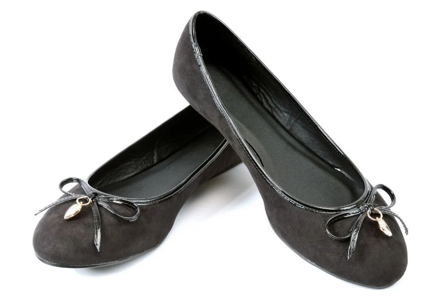 Pair of black suede ballet flats with patent-trimmed bows and small gold charms