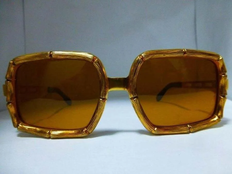 Vintage sunglasses with gold frames moulded like bamboo and brown tinted lenses, on a pale surface