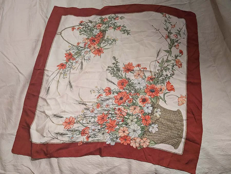 Vintage silk scarf spread flat, with a deep red border and a basket of red and white wildflowers