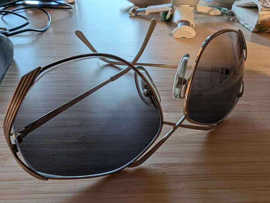 Vintage 1980s Dior sunglasses with thin gold-tone metal frames and grey gradient lenses, resting on a wooden table