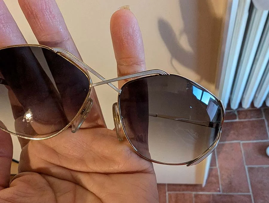 1980s Dior sunglasses held in an open palm, showing brown-grey gradient lenses in a fine gold-tone frame