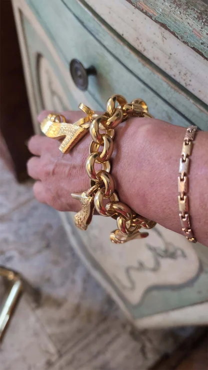 Heavy gold Ferragamo bracelet with small high-heel charms, worn on the wrist beside a flat gold link bracelet