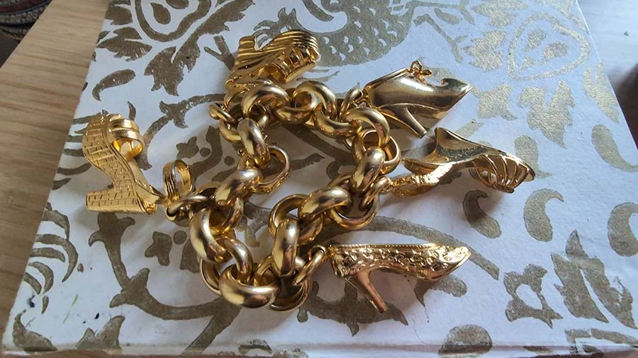Salvatore Ferragamo gold-tone charm bracelet hung with high-heel shoe charms, on a white box with a gold pattern