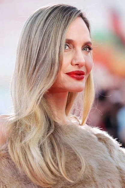 Close-up of Angelina Jolie in profile with long blonde hair, red lipstick and a fur stole at the Venice Film Festival