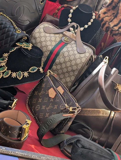 Vintage Louis Vuitton monogram and Gucci striped bags on a red stall, beside a necklace of green stones