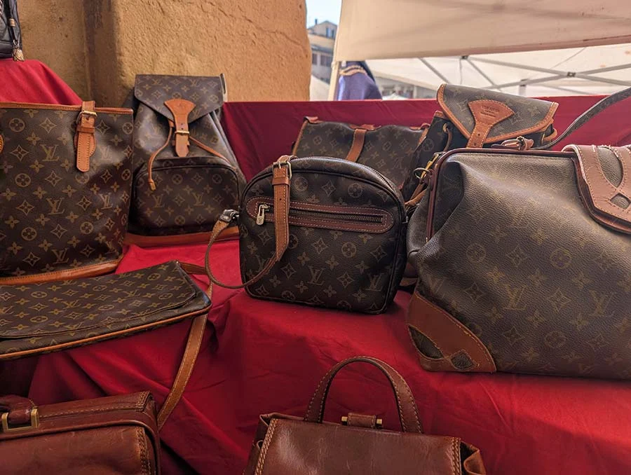 Vintage Louis Vuitton monogram bags of several shapes and a brown leather bag on a red cloth at a market