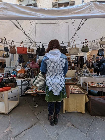 Gracie Opulanza from behind in a denim jacket with a white criss-cross panel, browsing a stall hung with handbags