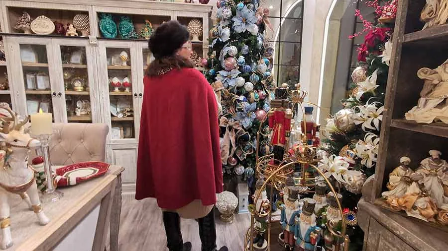 Gracie Opulanza in a red cape and black hat in a shop, beside a Christmas tree and toy nutcrackers
