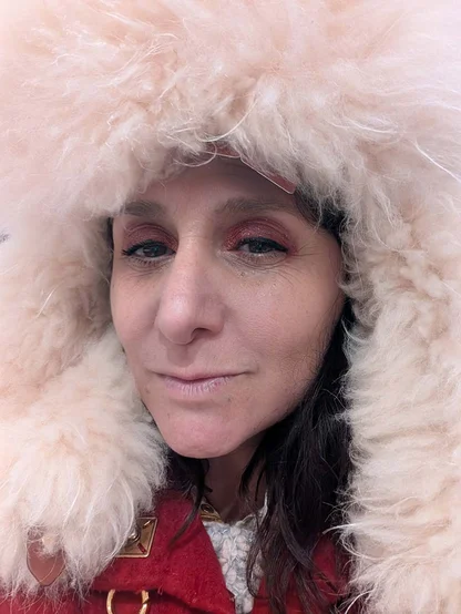 Gracie Opulanza in a pale pink lamb fur hood over a red coat