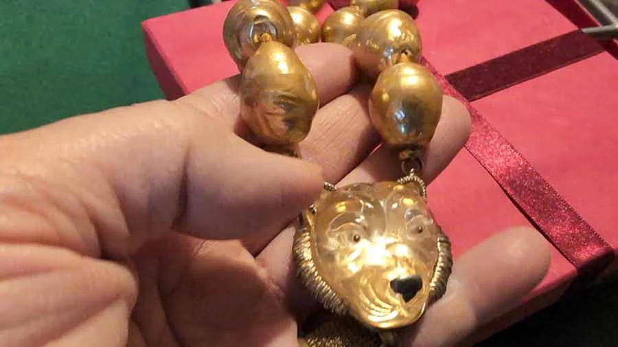 Strand of large golden baroque pearls with a gold lion's-head pendant, held in a hand over a red box