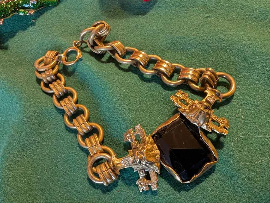 Gold-tone chain necklace with a large black stone and ornate metal fittings, laid on green velvet