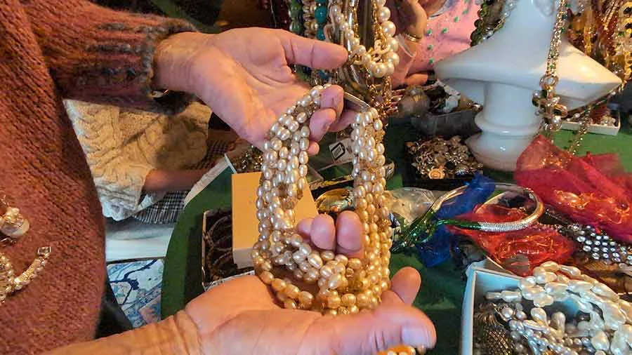 Hands holding up several strands of baroque pearls above a table of costume jewellery