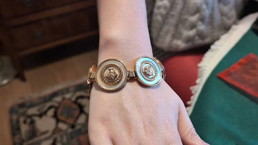 Gold-tone Versace bracelet with round embossed medallions in white and pale blue enamel, on a wrist