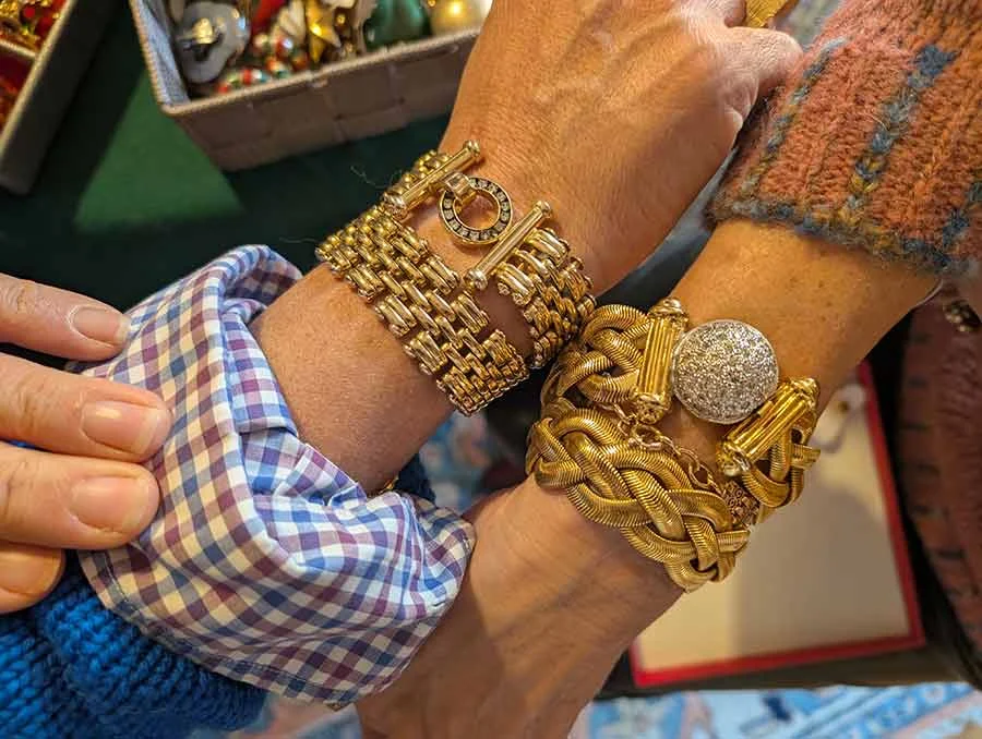 Two stacked gold-tone bracelets, one woven and one with a pavé disc, worn on crossed wrists