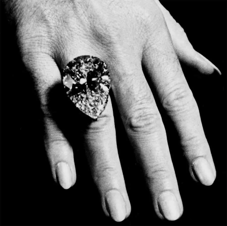 Black-and-white close view of a large pear-shaped diamond ring on a hand, bought from Cartier for Elizabeth Taylor