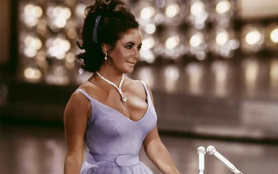 Elizabeth Taylor in a lilac V-neck dress at the Oscars, April 1970, wearing a necklace with a diamond pendant