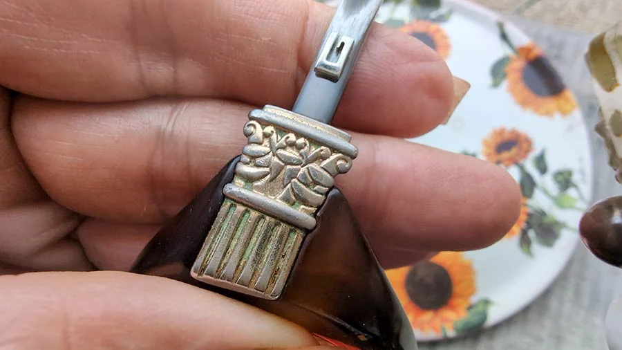 Silver-tone column detail on the vintage Gucci sunglasses, held between two fingers over a sunflower-print plate