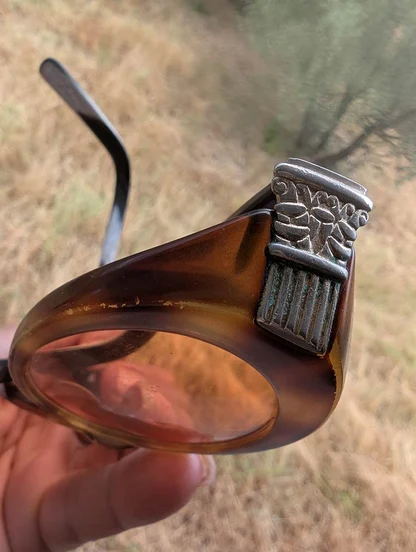 Side view of a vintage Gucci frame: amber-brown rim, tinted lens and a carved silver-tone column at the temple