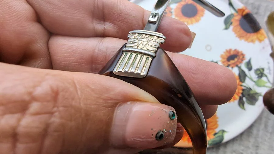 Hand holding the vintage Gucci frame: silver-tone ornament on a dark tortoiseshell temple, sunflower plate behind