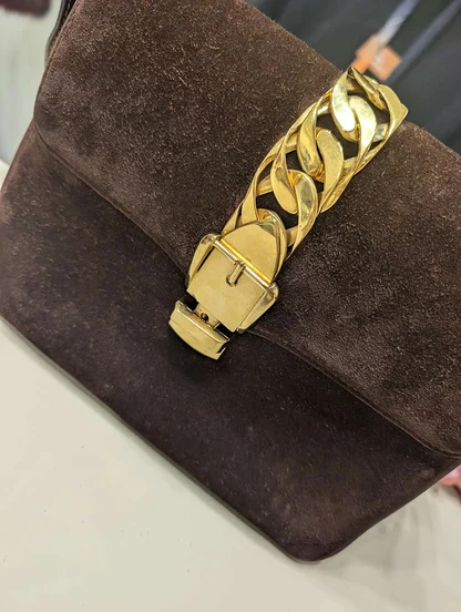 Close view of the suede flap with its heavy gold-tone chain and buckle, the bag's corner softly worn