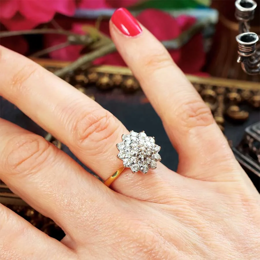 Woman's hand wearing a round diamond cluster ring on a yellow gold band, with red nail polish