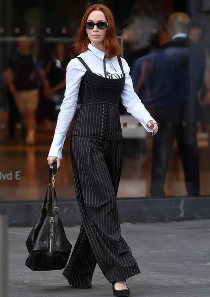 Woman in a white shirt, black pinstripe lace-up corset top and wide-leg pinstripe trousers, carrying a black leather bag