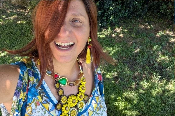 Woman laughing outdoors in a chunky yellow flower necklace with red and green stones and a yellow tassel earring