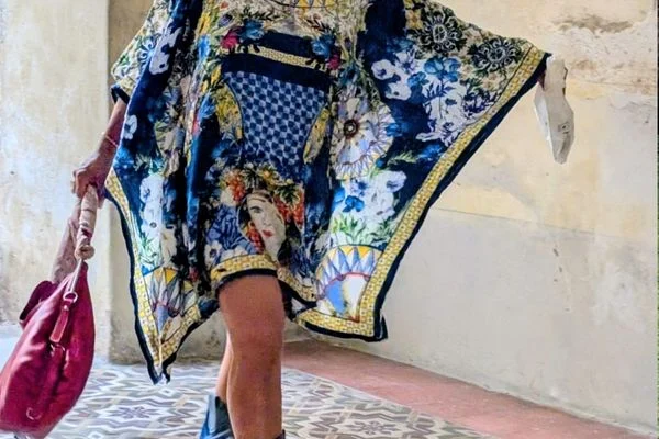 The red Tod's hobo bag held low by its strap, beside a blue and yellow printed kaftan